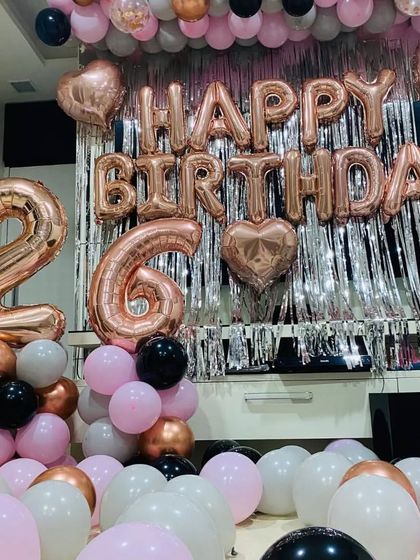 A popular rose gold, pink, and black theme for a 26th birthday, with a silver shimmer curtain and balloons filling the room.