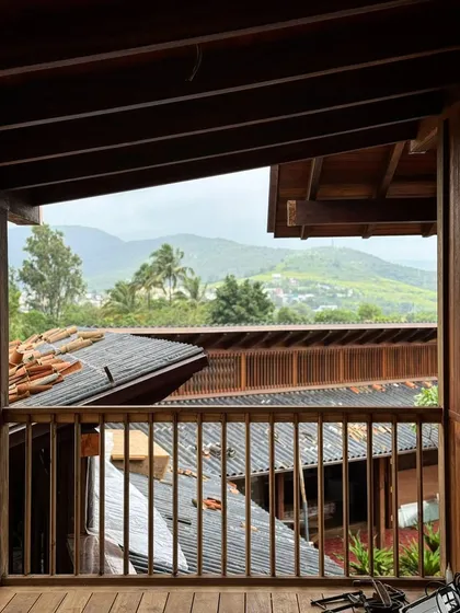 A view from an upper balcony during the monsoon season in Kamshet. The rich tones of the timber railings and roof structure are deepened by the rain, and the design provides ample protection while framing views of the hills.