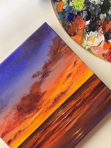 A vibrant sunset painting with a palette of orange, purple, and blue. The reflection of the sky on the water is created with quick, expressive brushstrokes.