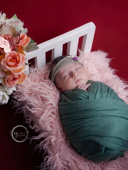 A close-up of a peacefully sleeping newborn, swaddled in green on a soft pink fur blanket. The details show the care taken in every shot.