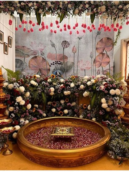 An elegant Haldi ceremony setup with a backdrop of lotus paintings and a large brass urli filled with petals for the ritual.
