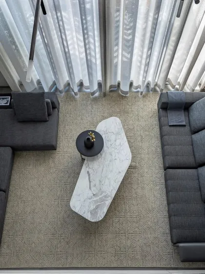 An overhead view of the living room, highlighting the geometric arrangement of the sectional sofa and the organic shape of the marble coffee table. This composition creates a balanced and inviting social space.