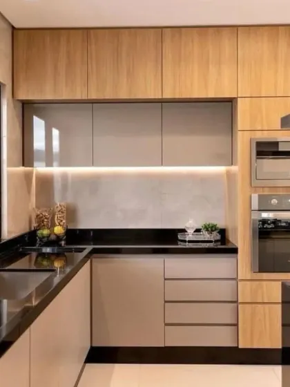 This design showcases a beautiful contrast between light wood cabinets and a sleek black granite countertop. The L-shaped layout includes an integrated oven tower and under-cabinet lighting, creating a functional and stylish kitchen.
