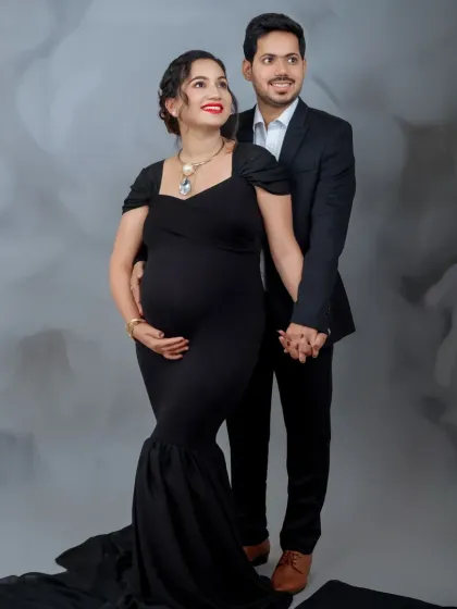 A sophisticated studio portrait of the couple. Their formal black attire against the textured grey backdrop creates a very chic and modern look.