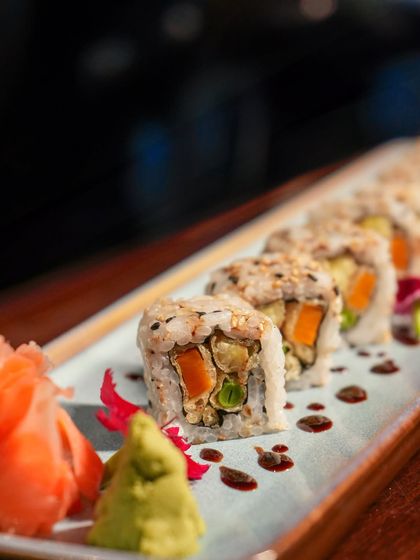 A close-up of our vegetable maki roll, served with traditional pickled ginger and wasabi. This roll is filled with a mix of fresh and cooked vegetables, offering a light and healthy option.