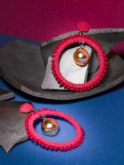 Pink hoop earrings styled with dark, rugged stones. The contrast between the soft, bright jewelry and the hard, dark props is visually striking.