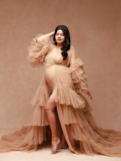 A full-length portrait showcasing the dramatic, floor-sweeping train and ruffled sleeves of this stunning nude-toned maternity gown.