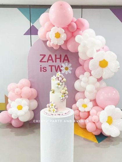 A sweet and simple daisy-themed second birthday. This setup uses a pink balloon arch decorated with balloon daisies around a personalized backdrop.