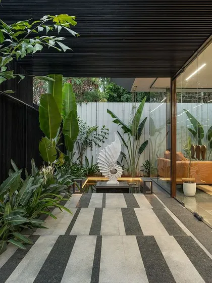An exterior view of the glass-box waiting lounge at Soul Spring. The design intentionally blurs the line between the built environment and the curated landscape, featuring a striped stone walkway and a prominent outdoor sculpture.