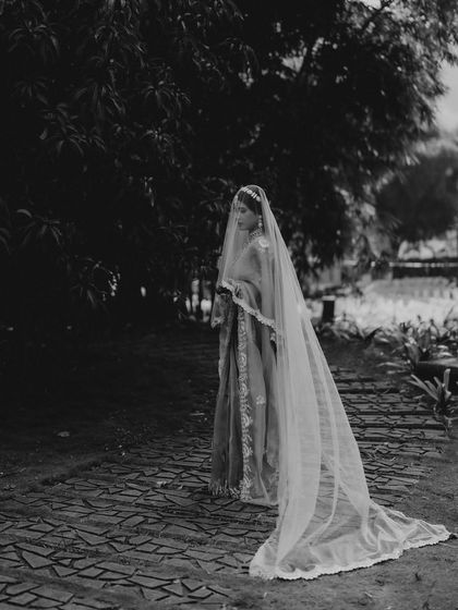A dramatic, full-length bridal portrait of Aishwarya. The long, flowing veil and the dark, moody background in this black and white shot create a truly artistic and timeless image.