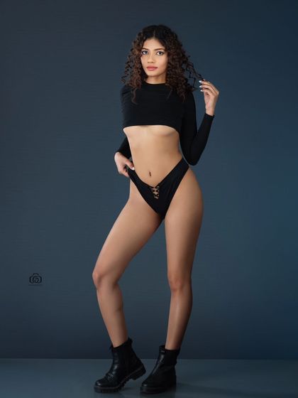 A minimalist studio portrait focusing on form and lines. The simple black outfit and boots against a clean grey background allow the model's pose and physique to be the central focus, ideal for a fitness or fashion portfolio.