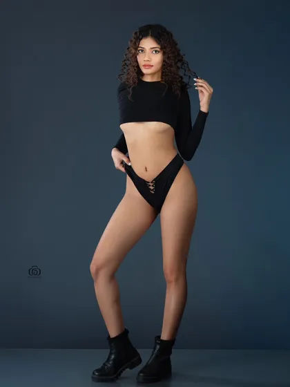 A minimalist studio portrait focusing on form and lines. The simple black outfit and boots against a clean grey background allow the model's pose and physique to be the central focus, ideal for a fitness or fashion portfolio.