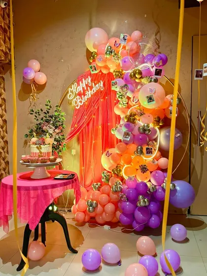 A unique and artistic birthday setup with a draped backdrop, a colorful balloon garland, and hanging polaroid photos.