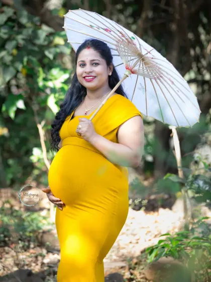 A joyful portrait with a traditional paper umbrella. The bright yellow dress and the cheerful prop add a touch of whimsy to this beautiful outdoor maternity photo.