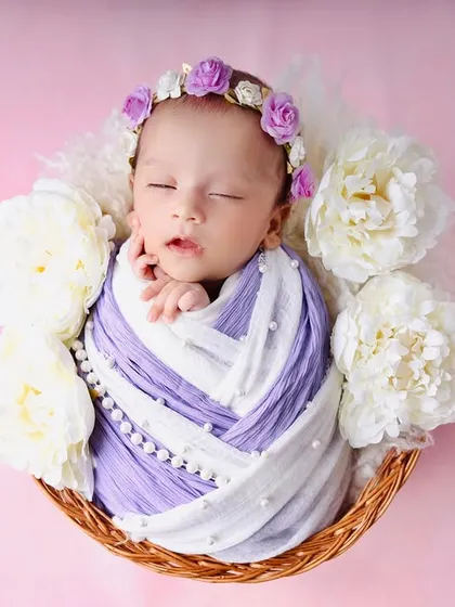 An overhead shot of the two-tone swaddled baby, nestled in a basket and surrounded by beautiful white peonies against a soft pink background.