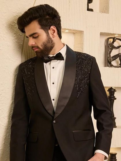 The same classic black tuxedo, viewed from a different angle to highlight the intricate shoulder detailing and the sharp contrast of the satin lapel against the suit fabric.
