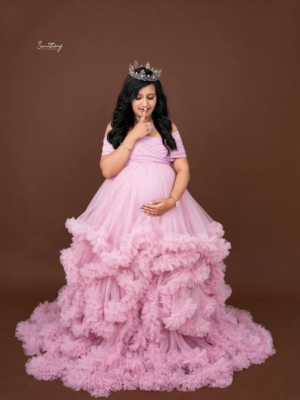 A playful and regal portrait of a mother-to-be in a pink ruffled gown and tiara. Her joyful expression and the rich color of the gown create a vibrant and happy image.