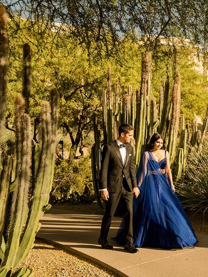 A walk through a cactus garden. The bride's electric blue lehenga provides a stunning pop of color against the desert landscape, complemented by the groom's timeless tuxedo.