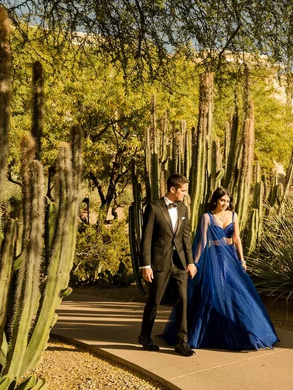 Walking hand-in-hand through a cactus garden, their formal reception attire creates a beautiful and unexpected contrast with the desert landscape.