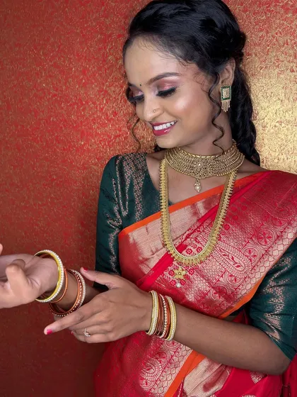 A candid shot of the client adjusting her bangles, showing the beautiful red saree and the glowing makeup.
