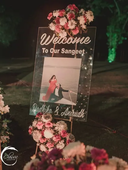 A personalized welcome to the Sangeet. This clear acrylic sign features the couple's pre-wedding photo, creating a warm and personal greeting for their guests.