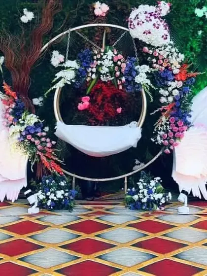 I design unique and modern cradle setups for naming ceremonies. This angel-wing themed 'thottilu' creates a heavenly centerpiece for your baby's special day, combining artistic cutouts with lush floral arrangements.