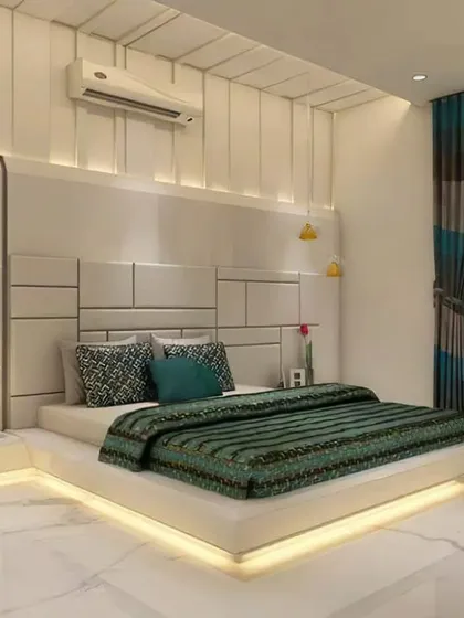 This luxurious master bedroom features a floor-to-ceiling upholstered headboard and a bed with an illuminated base. The combination of white marble floors and textured wall panels creates a bright and opulent feel.