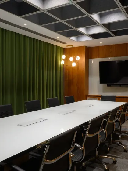 This meeting room proves that corporate spaces can have color. The rich green acoustic curtains not only help with sound but also add a bold, sophisticated touch against the warm wood paneling and modern grid ceiling.