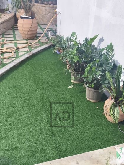 This project involved laying artificial grass in a curved garden space next to existing potted plants. The result is a consistently green lawn area that complements the real plants and is easy to keep clean.