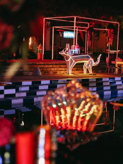 A glowing, geometric dog installation watches over the checkered pool, adding a playful and artistic element to this neon-lit cocktail party.