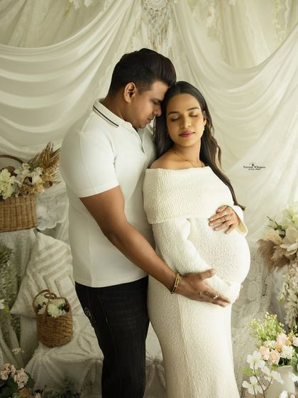 An intimate and loving portrait of a couple. They stand close together, both cradling the baby bump, in a moment of shared connection.