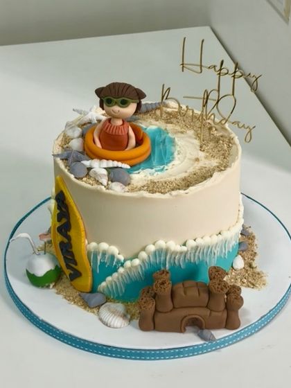 A beachy 3rd birthday! This cake brings the shore to the party with edible sand, waves, a sandcastle, and a custom fondant figurine enjoying the sun.