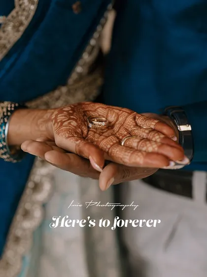 "Here's to forever." A close up shot focusing on the bride's hand, adorned with mehndi, holding the engagement ring in the groom's palm.