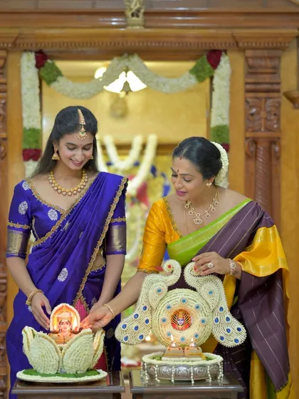A beautiful moment of two women lighting a traditional lamp, both dressed in our elegant silk sarees, celebrating our shared culture.