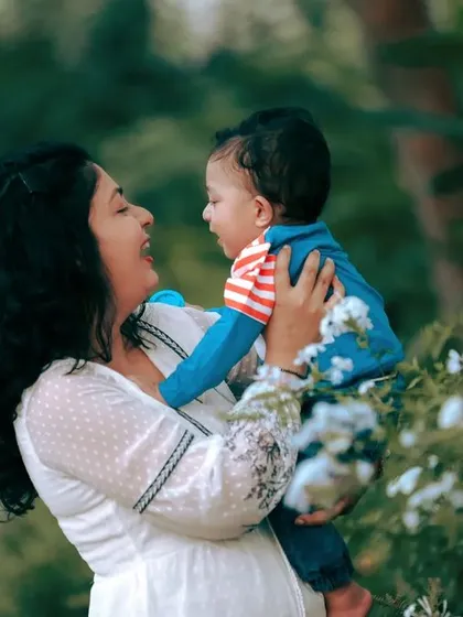 A mother shares a happy, playful moment with her baby boy. The natural green background and soft lighting are perfect for creating warm and authentic family photos.
