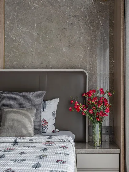 A close-up of a bedside table, where a grey marble wall panel provides a luxurious backdrop. The soft bedding with Indian motifs and a pop of color from fresh flowers adds a personal and warm touch.