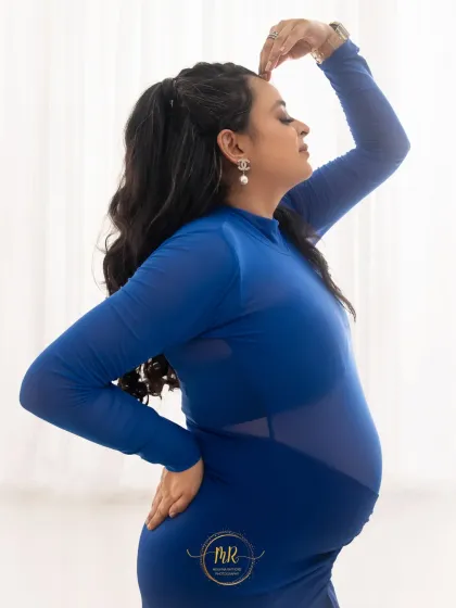 A confident and fashionable pose in a sheer-paneled blue maternity gown. This shot highlights a modern approach to pregnancy photography, focusing on style and form.