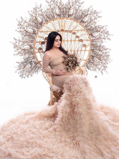 A regal portrait in the peacock chair, adorned with a beautiful floral arrangement. The client's beige ruffled gown spreads out magnificently, creating a stunning, high-fashion image.