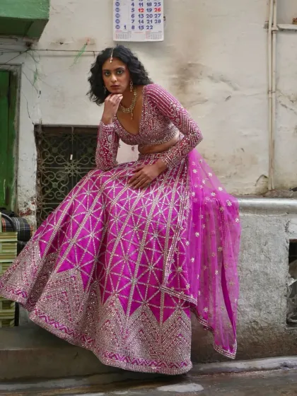 A pensive shot of the model in the pink geometric lehenga, highlighting its unique design and bold color.