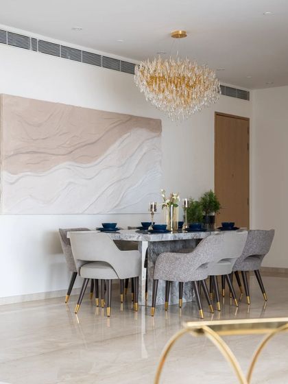 This dining room is a masterpiece of clean lines and refined elegance. A stunning crystal chandelier hangs above a solid marble table, while a large, textured art piece adds a layer of organic softness to the modern design.