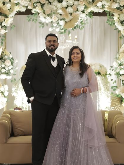 A full-length shot of the couple at their reception. The bride's makeup is designed to look stunning from a distance, with a clear focus on a radiant and happy glow.