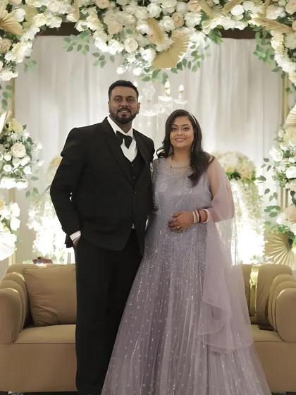 A full-length shot of the couple at their reception. The bride's makeup is designed to look stunning from a distance, with a clear focus on a radiant and happy glow.