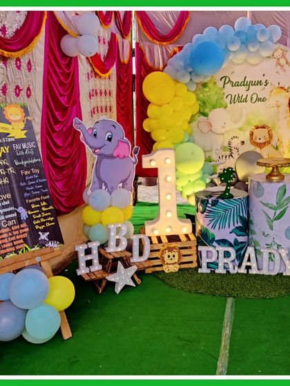 A "Wild One" jungle party setup with a personalized milestone board. This decor includes an elephant cutout, a faux grass floor, and a light-up number '1' for a memorable first birthday.