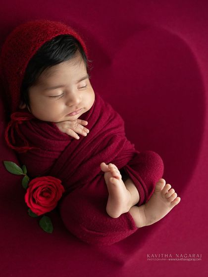 A newborn rests on a rich red backdrop, curled into a heart shape. This simple yet powerful image uses the color of love to celebrate a new life.