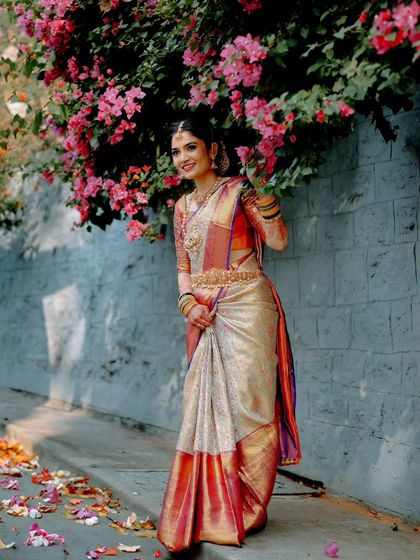The bride posing against a wall of pink flowers, creating a beautiful contrast with her cream and red saree. This is a perfect example of using natural elements for vibrant portraits.