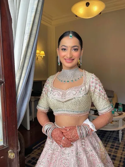 A happy bride ready for her daytime wedding. I created a sleek, clean bun and adorned it with a crown of pink flowers to match her lehenga.