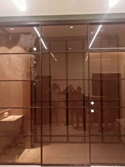 A full view of the sliding glass wardrobe system with its doors closed. The tinted glass provides a sleek, uniform look that enhances the modern feel of the room.