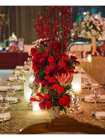A long dining table set with dramatic red floral centerpieces and warm lighting. This demonstrates our ability to create a bold and passionate ambiance through coordinated decor and lighting for evening events.