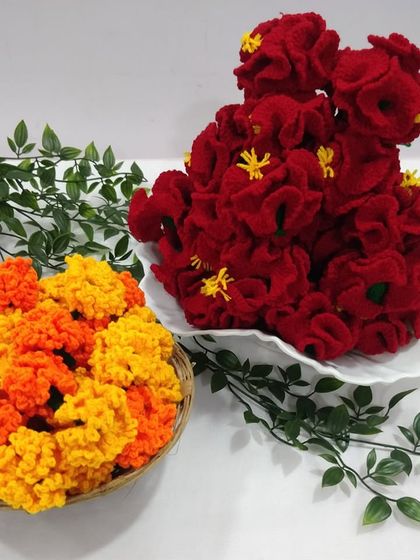 An assortment of my crochet flowers, including vibrant orange and yellow marigolds and deep red hibiscus flowers.