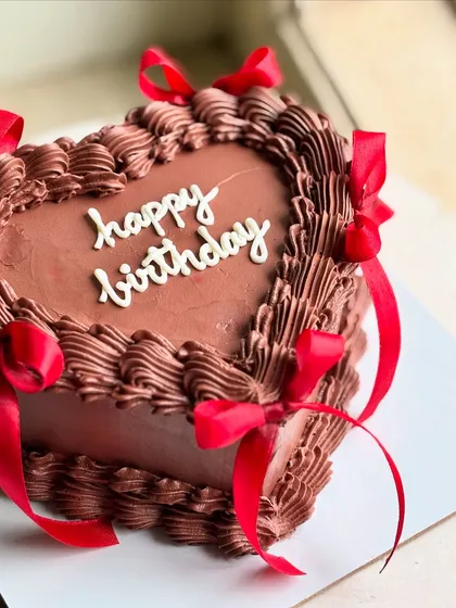 Too cute to eat, too pretty not to post. A rich chocolate heart cake with detailed piping and bold red satin ribbons, perfect for a classic and romantic birthday celebration.